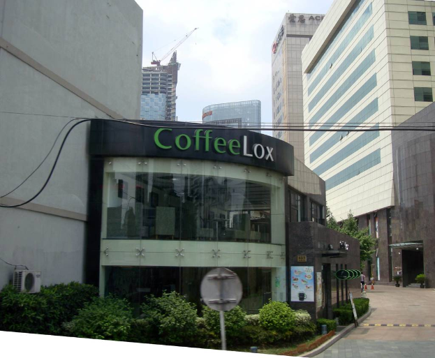 Ein Geschäftsgebäude mit einigen Pflanzen davor, umgeben von vielen hohen Gebäuden und Drähten.