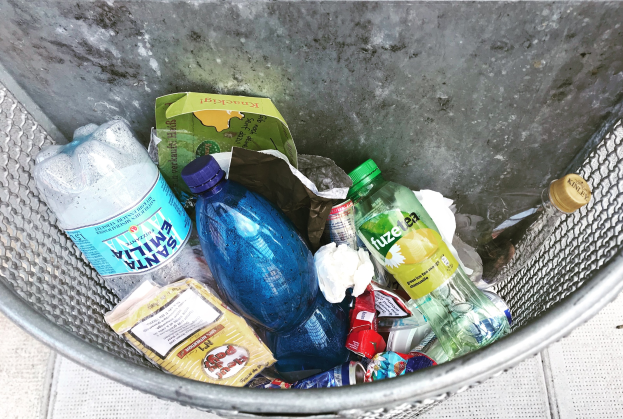 Ein Metallmüllcontainer voller Plastikflaschen, Tüten und anderer Gegenstände.