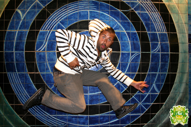 Ein Mann tanzt vor einem bunten Hintergrund mit einem Logo, das Text in der rechten oberen Ecke enth├Ąlt.