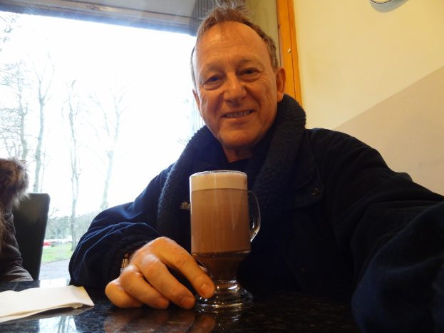 Ein Mann sitzt drinnen mit einem Bierglas vor ihm, mit Bäumen und Gras sichtbar außerhalb des Raumes.