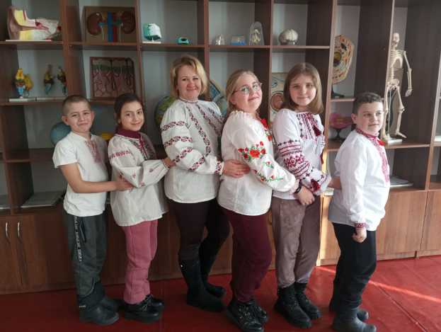Eine Gruppe von Kindern in traditioneller ukrainischer Kleidung steht zusammen vor einem Regal voller Spielzeuge, einem Skelett und anderen Gegenständen.