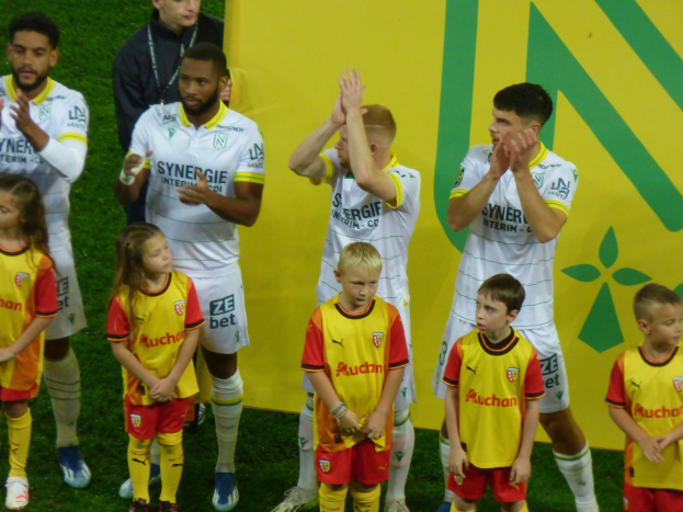 Eine Gruppe von Fußballspielern in Uniformen klatscht feierlich auf einem Ligue-1-Feld, mit einem "Ligue-1" Schild im Hintergrund.