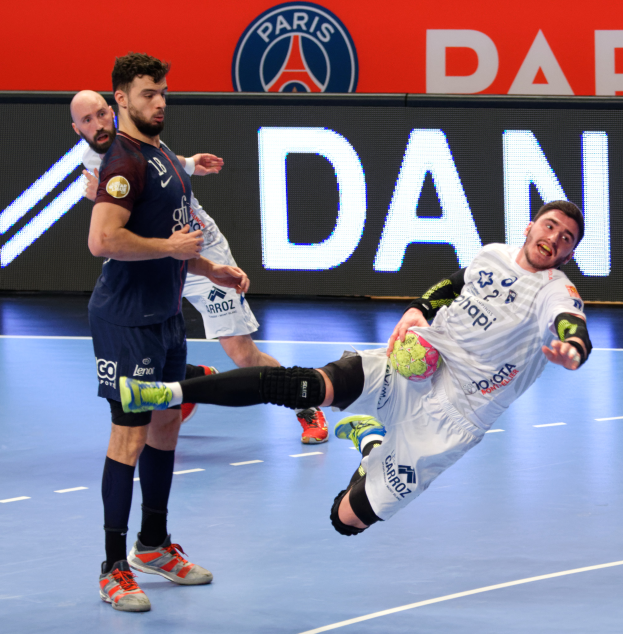 Eine Gruppe von Männern, die Handball auf einem Platz spielen, einer hält den Ball, mit einem Paris Saint-Germain-Futsal-Team-Schild im Hintergrund.