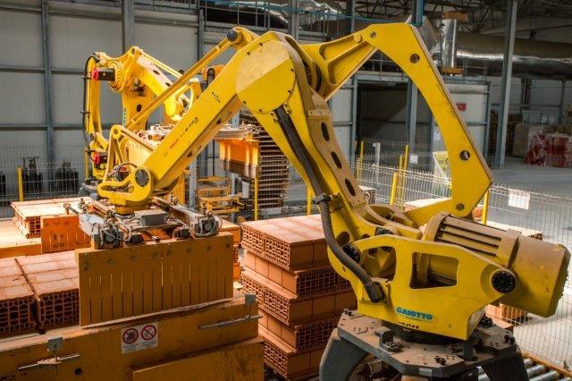 Großes Industrie-Lager mit gestapelten Kisten, Kränen, Zäunen, Pfählen und einer fernen Wand in einer automatisierten Fertigungsumgebung.