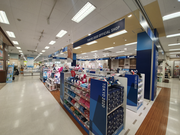 Das Innere eines offiziellen Tokyo 2020-Shops mit Kleidung auf Gestellen, Namensschildern, Deckenlampen und verschiedenen anderen Gegenständen.