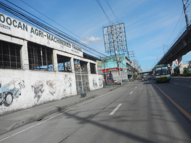 Stadtstraße mit fahrenden Fahrzeugen, eine Brücke auf der rechten Seite, Gebäude, Strommasten mit Drähten, ein bewölkter Himmel und ein graffiti-beschmiertes Gebäude an der Seite.