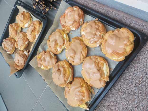Ein Tablett mit verschiedenen dänischen Keksen, einige davon mit Puderzucker bestäubt, steht auf einer Theke neben einem offenen Fenster und wird von warmem Licht beschienen.