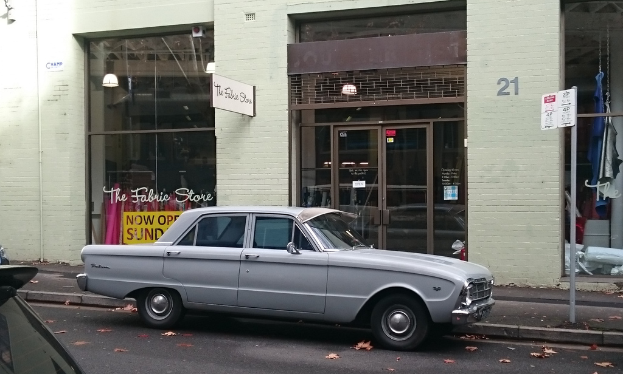 Ein silberfarbenes Auto parkt auf der Straße vor einem Gebäude mit mehreren Türen, und ein Schild ist an einem nahen Pfahl zu sehen.
