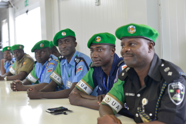 Gruppe von Polizeibeamten, die an einem Tisch während einer Schulung sitzen, mit Mobiltelefonen und anderen Gegenständen auf dem Tisch, in einem Raum mit Fenstern und Deckenbeleuchtung.