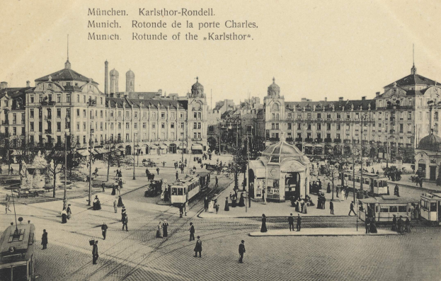 Ein Schwarz-Weiß-Foto einer belebten Stadtstraße in Karlsthor-Rondell, Deutschland, mit Menschen, Fahrzeugen, Pfählen, Bäumen und Gebäuden mit Fenstern und auf dem Bild geschriebenem Text.