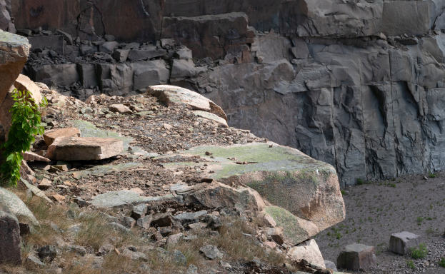 Eine felsige Hügellandschaft mit einer markanten Felsformation in der Mitte, umgeben von Gras und kleinen Pflanzen.