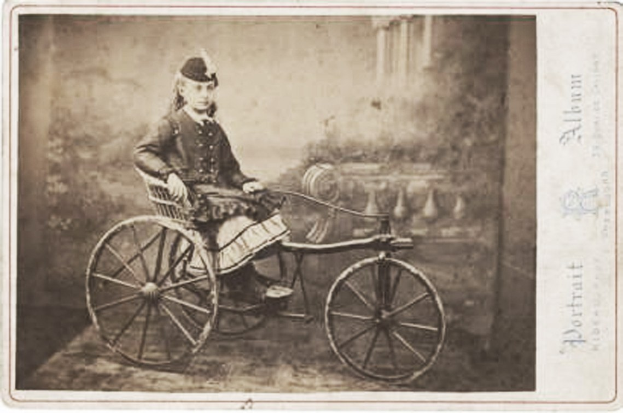 Schwarzes und weißes Foto einer Frau in einem Kleid und einer Kappe, die auf einem Fahrrad sitzt, mit Text auf der rechten Seite.