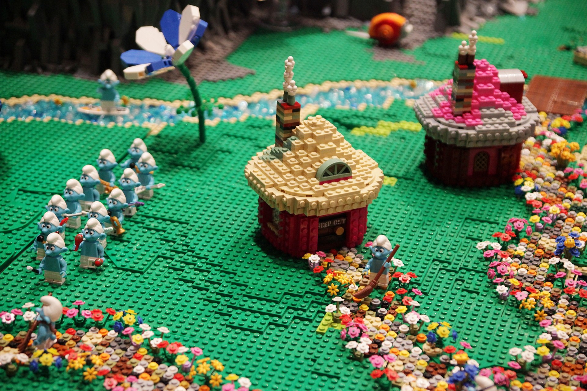 Ein LEGO-Modell einer Kleinstadt mit bunten Blumen, Häusern, Pflanzen und Spielzeugen vor einem leicht unscharfen Hintergrund.