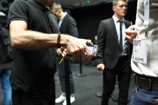 Eine Person in einem Hemd und eine andere in einem Anzug stehen vor einem schwarzen Hintergrund, eine hält ein Objekt und trägt eine ID-Karte.