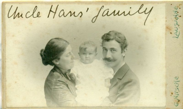 Ein altes Foto eines Mannes im Anzug und Krawatte, einer Frau, die ein Baby hält, mit der Aufschrift "Onkel Hans' Familie" oben drauf, alle mit warmherzigen und liebevollen Gesichtsausdrücken.