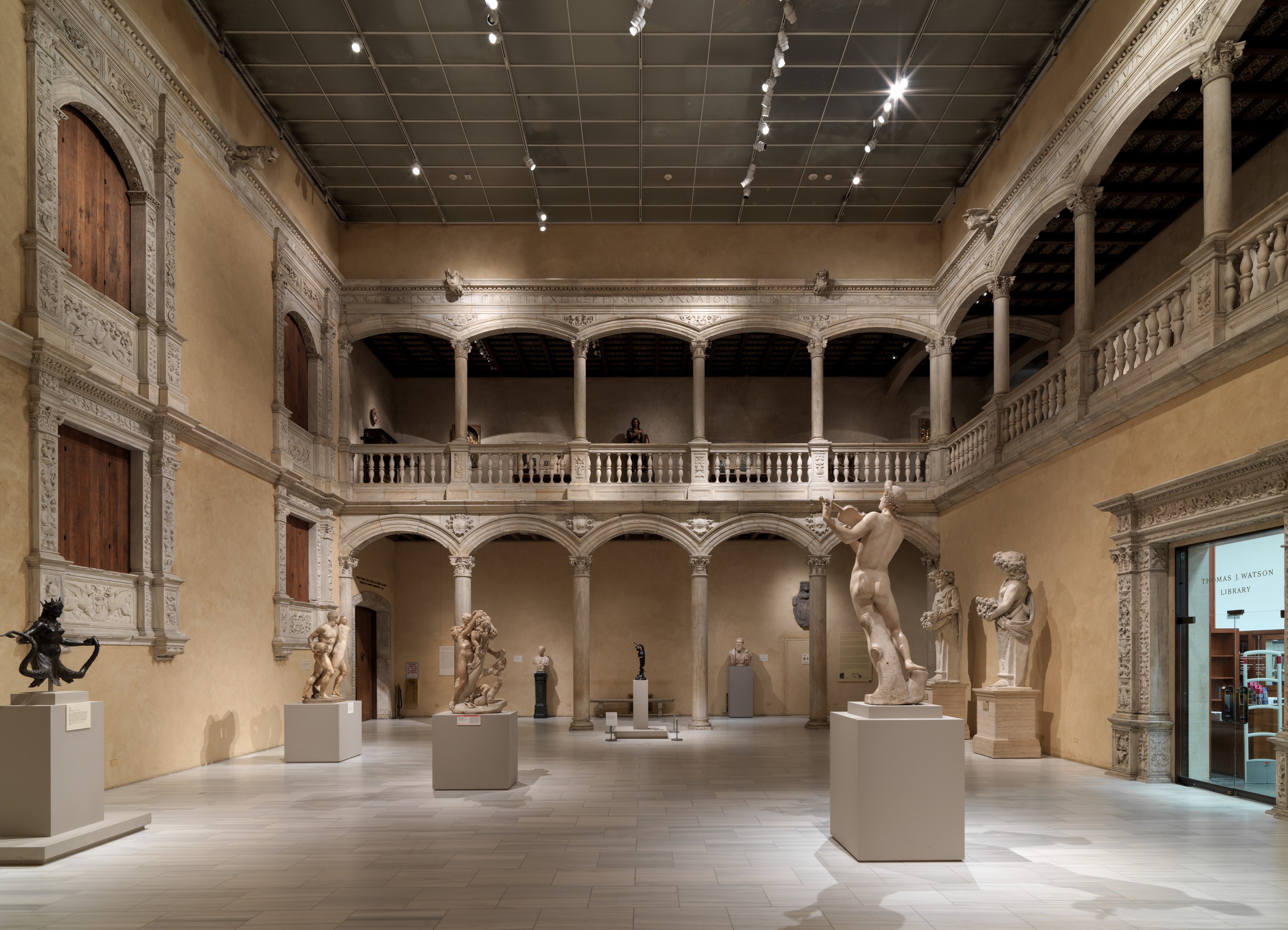 Großer Raum in einem Museum voller Statuen und Skulpturen auf Sockeln, mit Menschen, die die Ausstellungen beobachten.