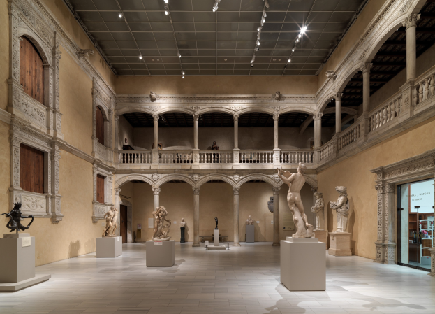 Großer Raum in einem Museum voller Statuen und Skulpturen auf Sockeln, mit Menschen, die die Ausstellungen beobachten.