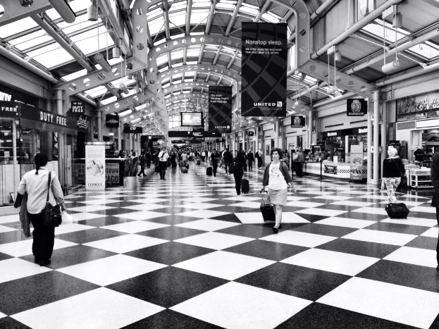 Menschen mit Taschen gehen in einem Gebäude mit Läden und Bannern auf der Seite.