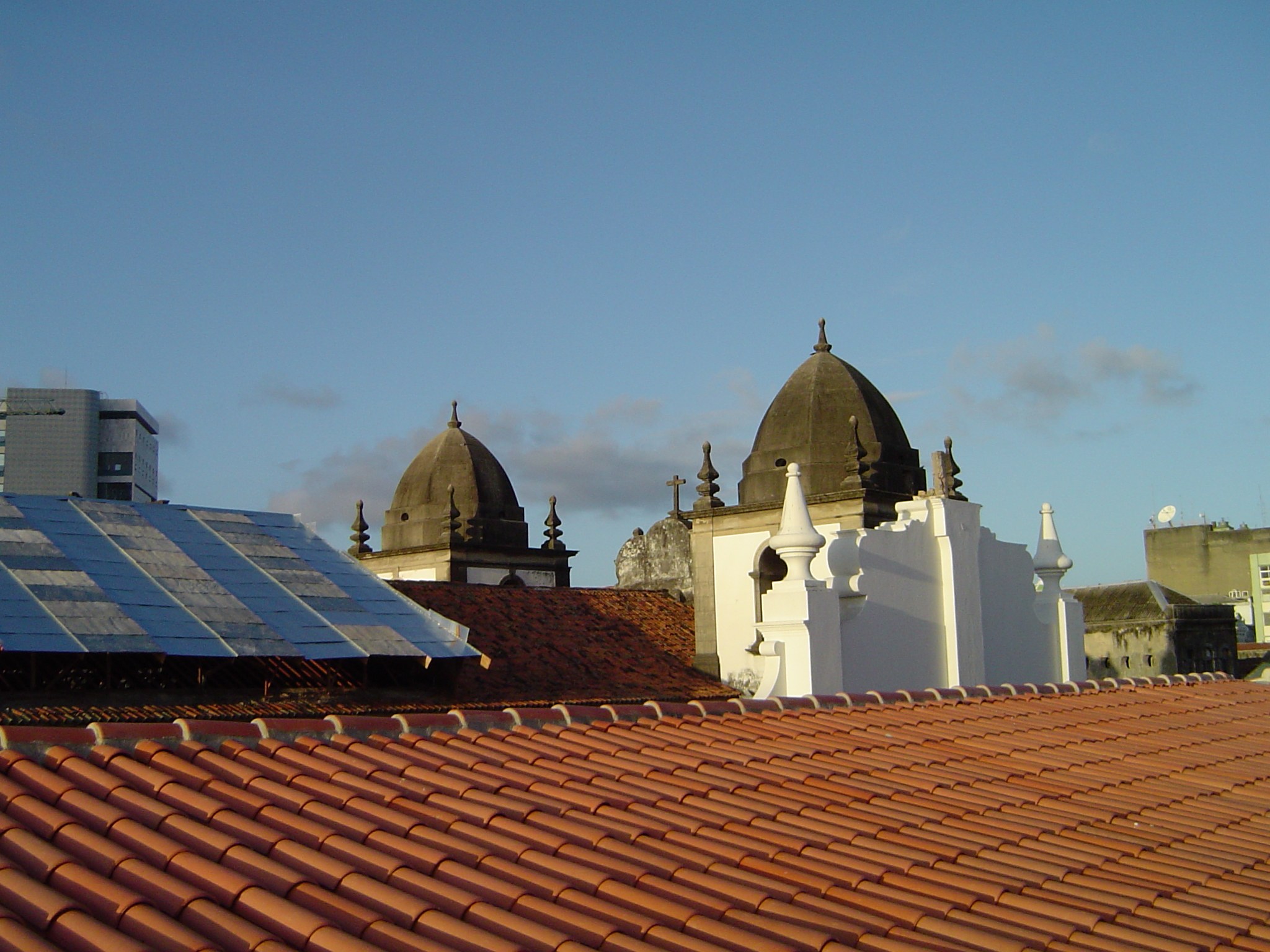 Stadtansicht mit mehreren Gebäuden im Vordergrund, einem blauen Himmel im Hintergrund und Solarpanelen auf dem Dach eines Gebäudes.