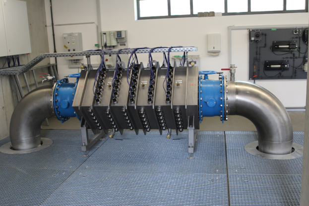 Großer industrieller Wärmetauscher in einem Gebäude mit Fenstern, verbunden mit verschiedenen Komponenten und Kabeln.