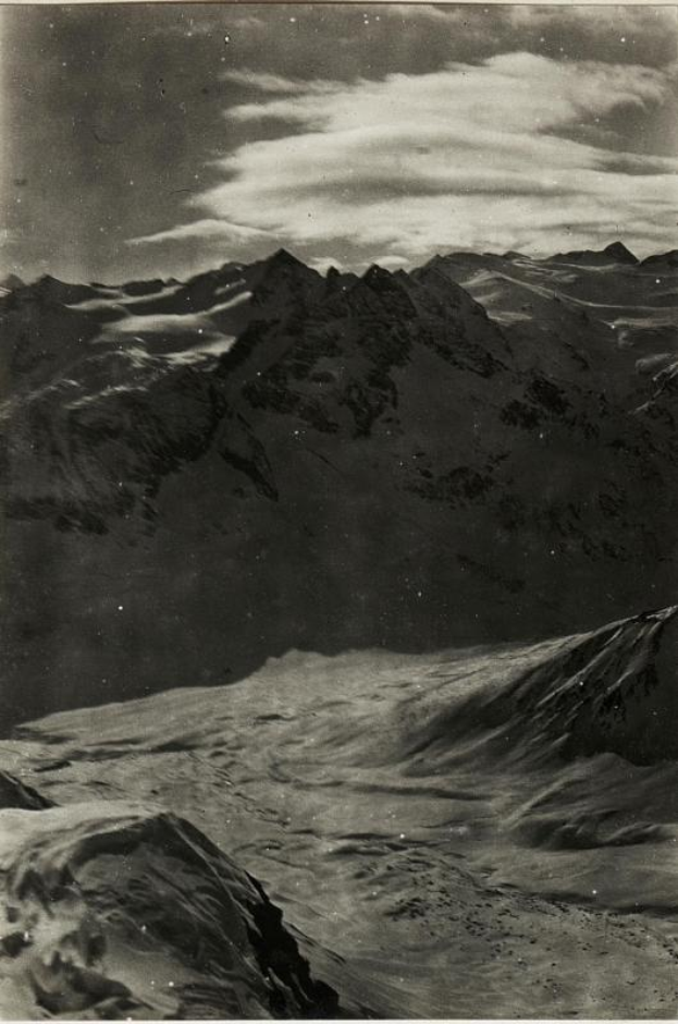 Ein Schwarz-Weiß-Foto einer schneebedeckten Gebirgslandschaft mit einem bewölkten Himmel und einem Text am unteren Rand, der 'Gustav Klimt - Die Alpen' lautet.