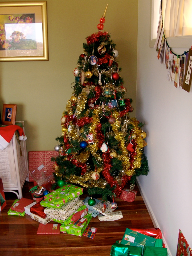 Ein geschmückter Weihnachtsbaum auf der rechten Seite mit Geschenken am Fuße, ein Foto Rahmen an der linken Wand und ein Vorhang am rechten Fenster.