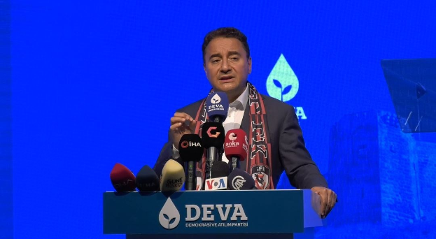Mann an einem Rednerpult mit Mikrofonen, tragend einen Mantel und eine Mütze, sprechend auf einer Veranstaltung mit einem Bildschirm und einem Gegenstand im Hintergrund; Text auf dem Pult lautet "deva-Geschäftsführer sagt, es sei keine gute Idee für die Zukunft"