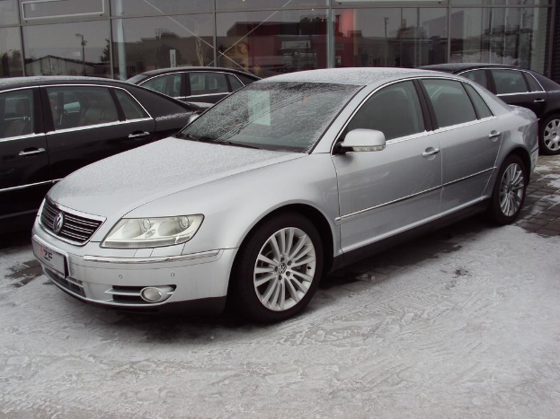 Ein Auto steht auf einem verschneiten Gehweg vorne, mit drei Autos und einem Glasgeb√§ude im Hintergrund.