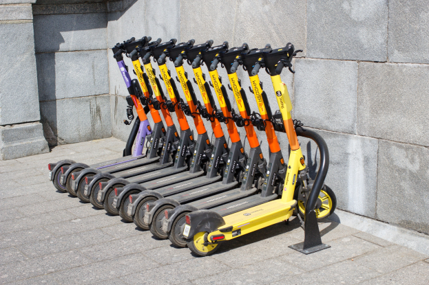 Eine Reihe von Elektro-Scootern ordentlich auf einem Bürgersteig geparkt mit einer Wand im Hintergrund.