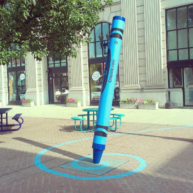 Ein Geb√§ude mit T√ľren in der Mitte, einem Baum oben links und B√§nken in der Mitte.