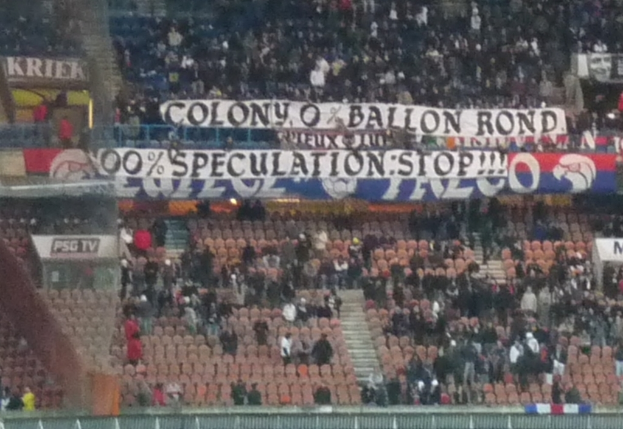 Ein Stadion voller Menschen, Fahnen und Stühle, mit einem Zaun unten und Treppen auf der linken Seite.