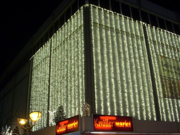 Ein Gebäude in Berlin, Deutschland, geschmückt mit Weihnachtslichtern, umgeben von Bäumen, Laternenmasten und Schildern mit Text, mit dem Himmel im Hintergrund.