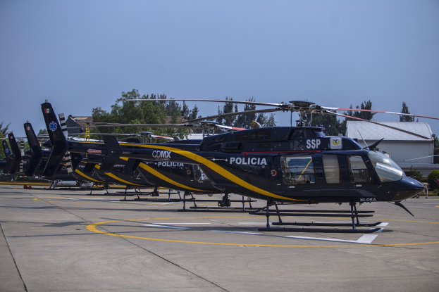 Polizeihubschrauber auf einem Flughafenvorfeld mit umliegenden Gebäuden, Bäumen und einem klaren blauen Himmel.