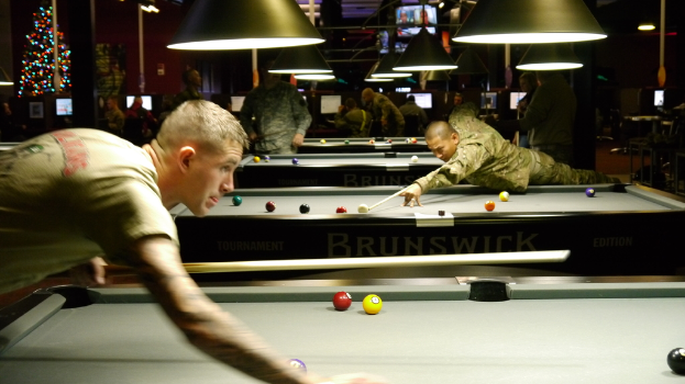 Ein Raum mit Snookertischen, Spielern auf beiden Seiten, hängenden Lampen, einem Weihnachtsbaum in einer Ecke und Bildschirmen, die Ergebnisse anzeigen.