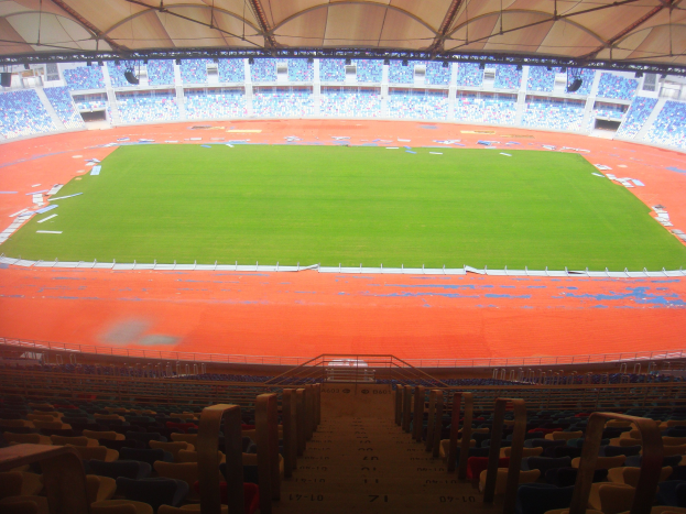Ein großes Stadion voller Zuschauer, mit mehreren Sitzreihen, Geländern, Treppen und einem Dach, mit dem Spielfeld in der Mitte sichtbar.