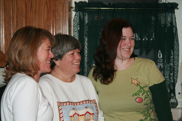 Frauen im Vordergrund stehend und lachend mit einer Wand, grünem Vorhang und holzem Fenster im Hintergrund.
