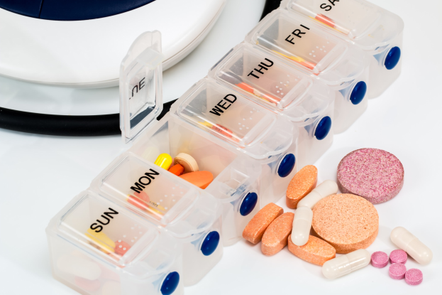 Weißer Tisch mit einem Pillenschächtelchen, das Pillen enthält, und einem Stethoskop daneben, das Pillenschächtelchen mit Text beschriftet.