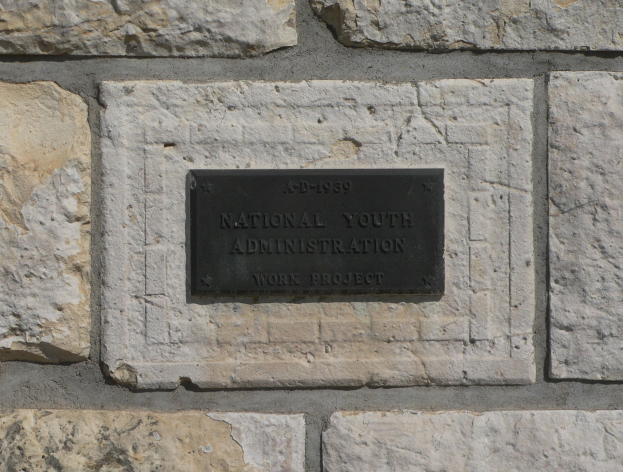 Steinwand mit einem rechteckigen Schild, auf dem "National Youth Administration" in weißer, fetter Schrift auf einem schwarzen Hintergrund steht.