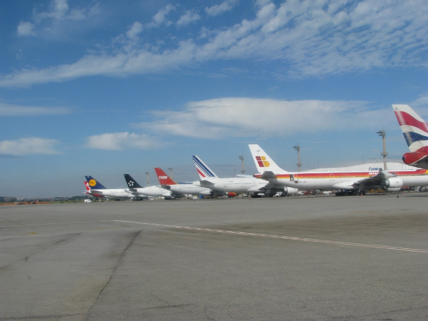 Mehrere Flugzeuge befinden sich auf einer Start- und Landebahn mit Masten, Kabeln und Wolken am Himmel.