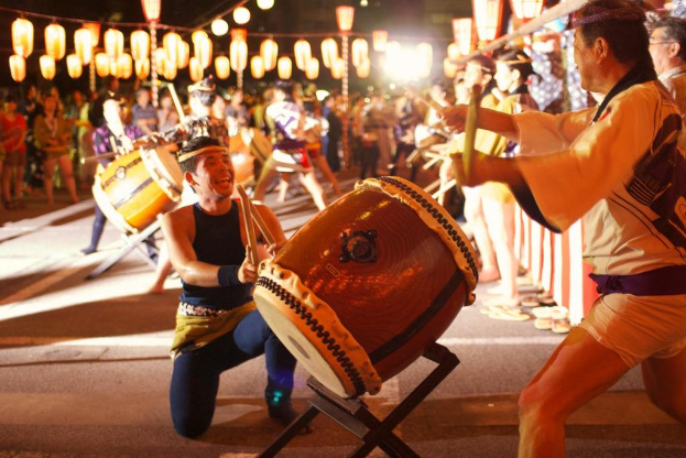 Männer spielen Trommeln auf einem Festival mit Lichtern darüber.