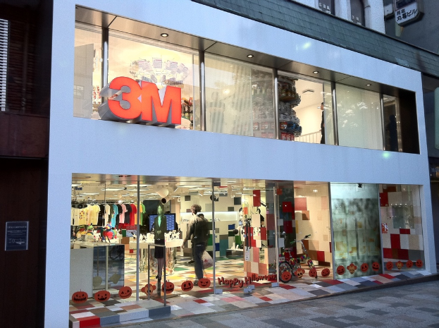 Ein Gebäude mit einer Glaswand, auf der Kleider an Bügeln hängen, eine Schaufensterpuppe, ein Fahrrad, aufgeklebte Bilder und Schrift auf dem Glas.