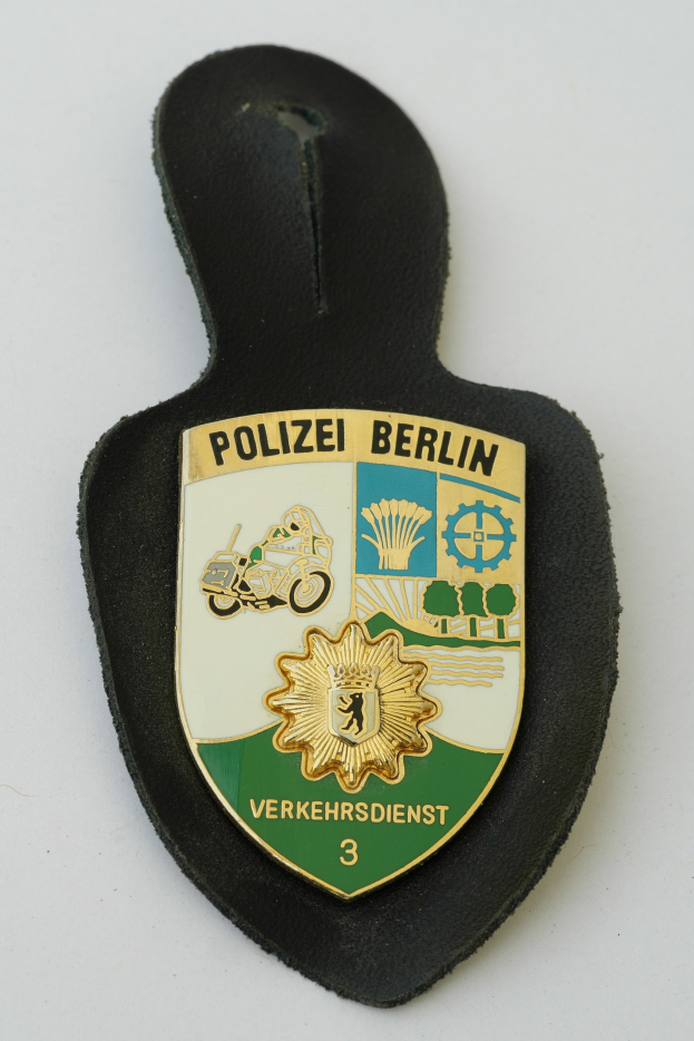 Polizei Berlin Abzeichen mit einem blauen Schild, weißer Stern und schwarzem Text auf einem weißen Rand, auf einer Oberfläche platziert.