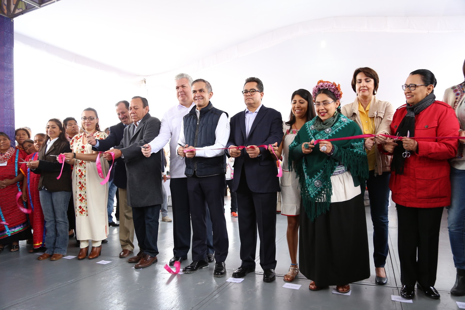 Eine Gruppe von Menschen, die bei einer Scherenschnitte-Zeremonie lächeln, mit Scheren in der Hand und Papieren auf dem Boden und einem weißen Tuch im Hintergrund.
