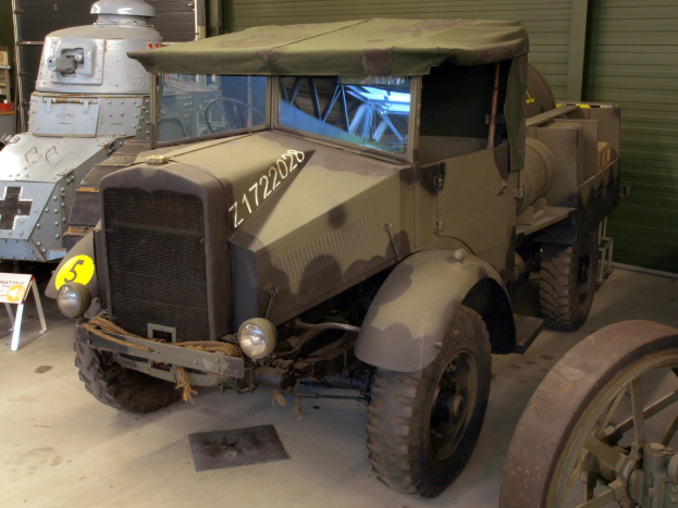 Alter Militärlastwagen in einer Garage neben anderen Militärfahrzeugen geparkt, mit einer Tafel mit Text auf dem Boden, Rollläden und anderen Gegenständen im Hintergrund.