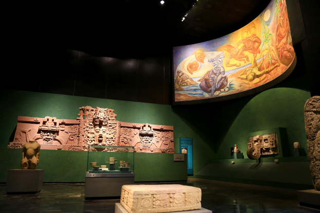 Ausstellung von verschiedenen Artefakten im Anthropologischen Museum von Mexiko-Stadt, darunter Skulpturen, Tischgegenstände, eine Texttafel, eine Wandmalerei und Deckenleuchten.