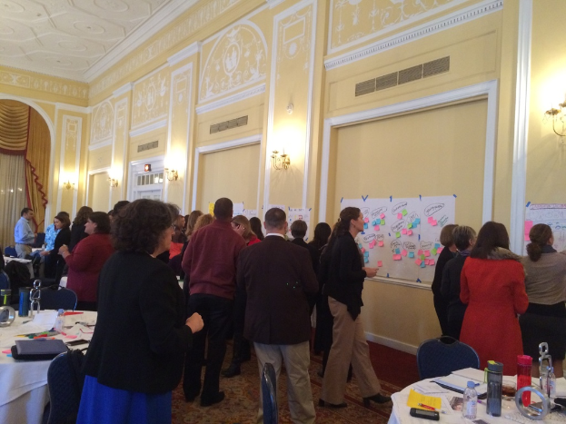 Eine Gruppe von Menschen untersucht Plakate und Schaubilder an einer Wand in einem, was wie ein Kunstmuseum aussieht.