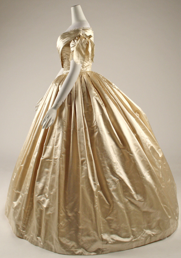Eine Schaufensterpuppe in einem Museum präsentiert ein goldenes Ballkleid mit hohem Ausschnitt, langen Ärmeln, einer taillierten Taille und einem weiten, bauschigen Rock.