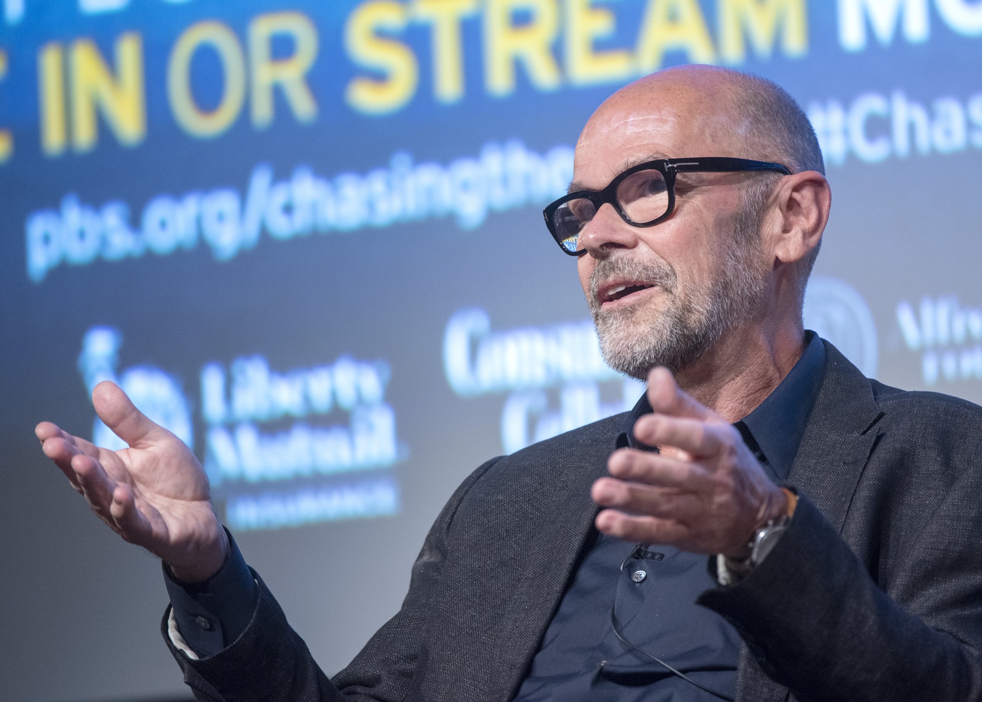 Steve Ballmer, Gründer und CEO von PBS, spricht in ein Mikrofon mit einem Bildschirm im Hintergrund.