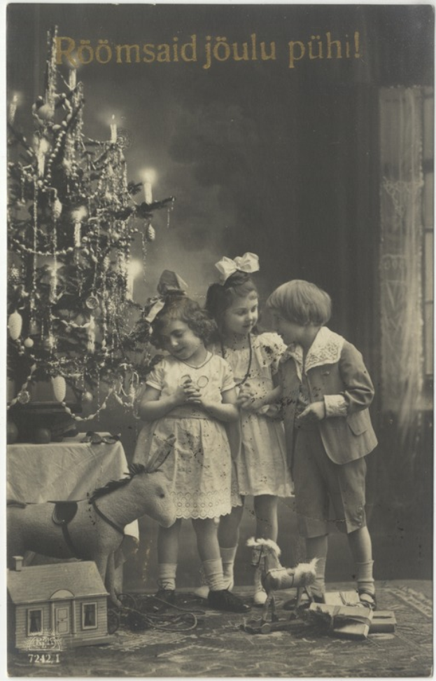 Ein altes Foto von drei Kindern, die vor einem geschmückten Weihnachtsbaum stehen, mit einem Tisch auf der linken Seite und verstreuten Spielzeugen auf der rechten Seite und Text oben.