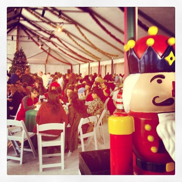 Eine Gruppe von Menschen feiert Weihnachten in einer Hütte, mit einem geschmückten Baum, weißen Stühlen, einem roten Spielzeug-Sicherheitsmann und einer schwarzen Krone.